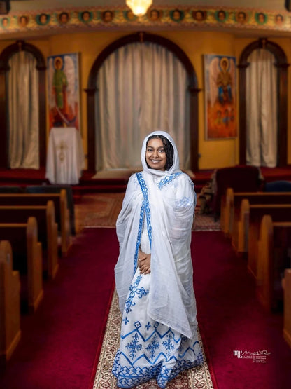 Woman in a white and blue traditional Habesha Kemis  standing in a church.