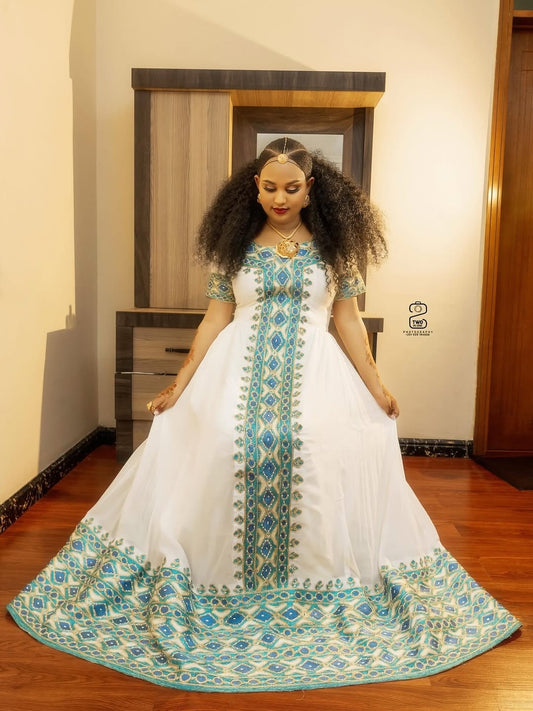 Woman wearing a white Ethiopian Libs with blue embroidery in a room.