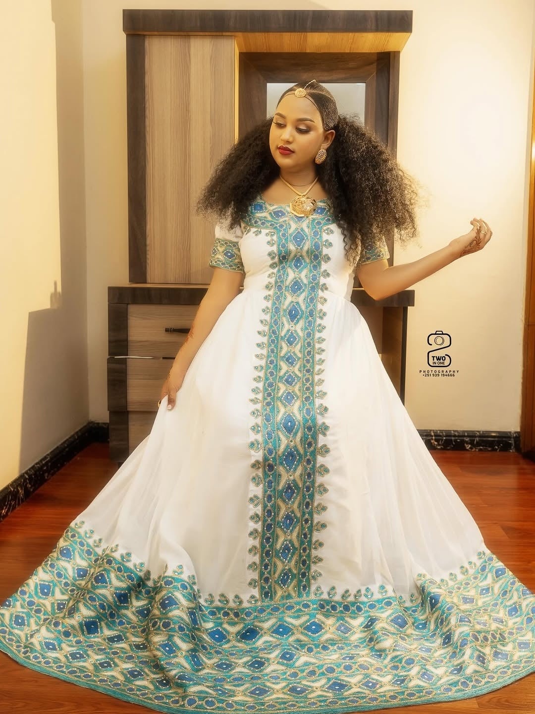 Woman wearing a white Ethiopian Libs with blue and green patterns indoors.