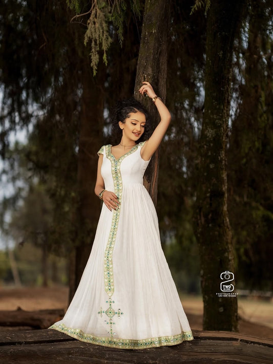 Woman in a white Ethiopian Kemis with green embroidery standing under a tree