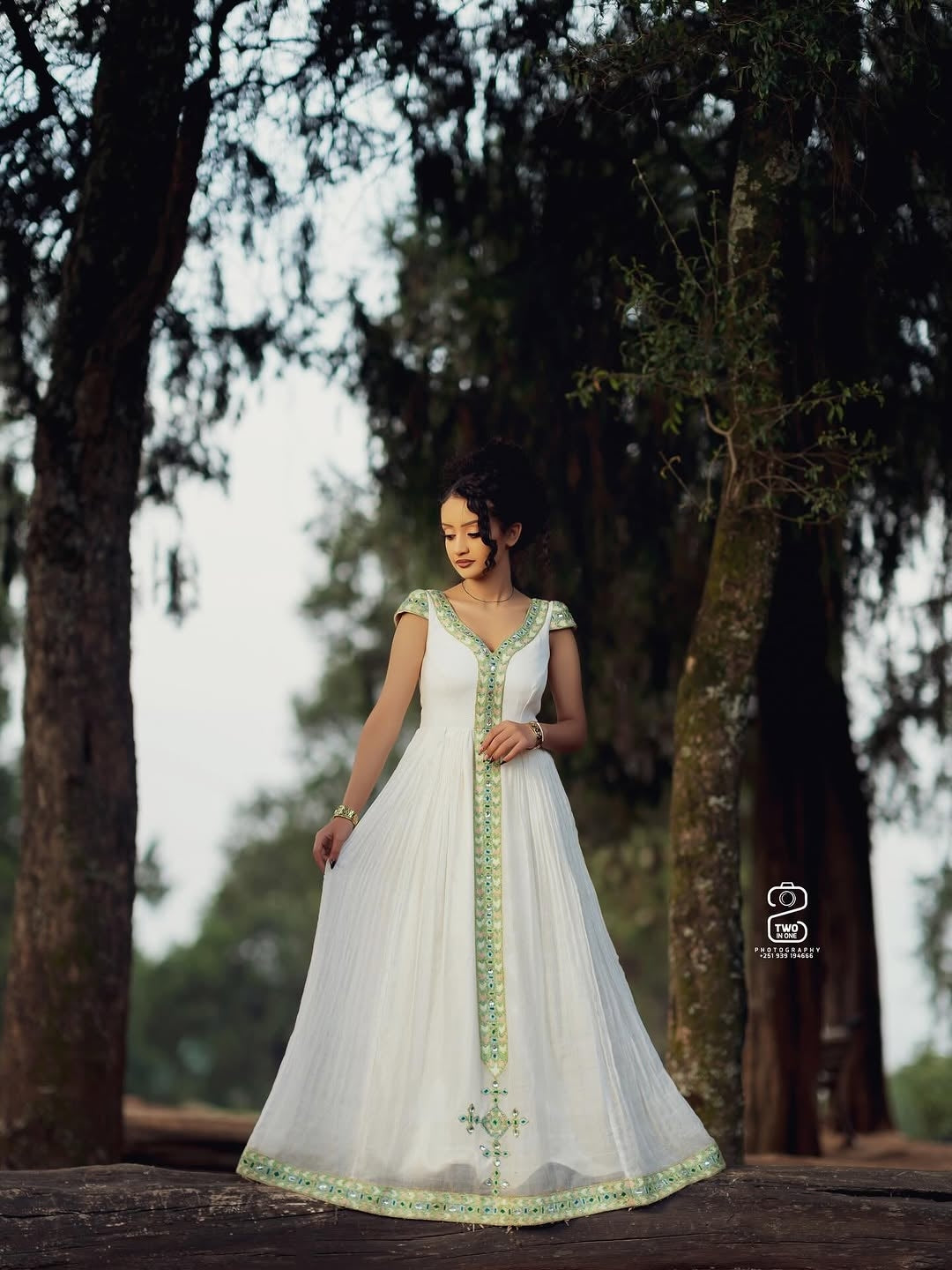 Woman in a white Ethiopian Kemis with green embroidery standing in a forest setting