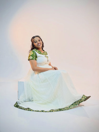 Woman in a white and green Ethiopian Traditional Dress sitting on a white background