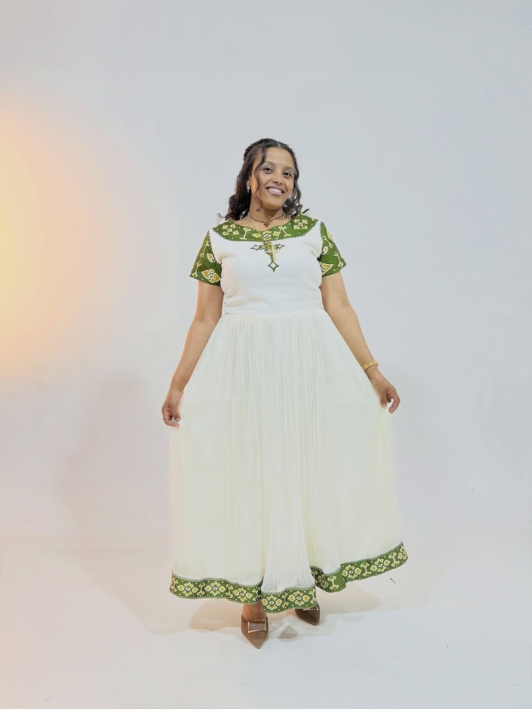 Woman wearing a white Ethiopian traditional dress with green embroidery on a plain background
