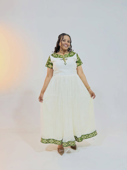 Woman wearing a white Ethiopian traditional dress with green embroidery on a plain background