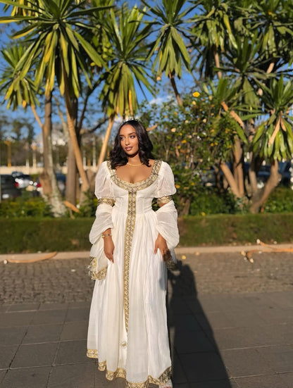 Woman in a white Habesha Zuria with gold details standing outdoors with palm trees in the background