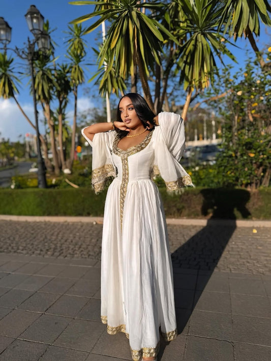 Woman in a white and gold Habesha Zuria standing outdoors with greenery in the background