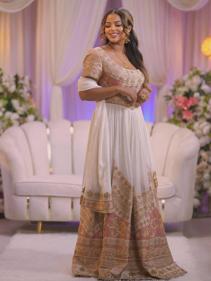 Woman in a traditional outfit standing in a decorated room with floral arrangements and white furniture.