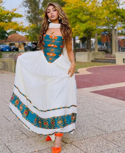 Woman in a white and Teal Ethiopian Dress with orange shoes standing outdoors.