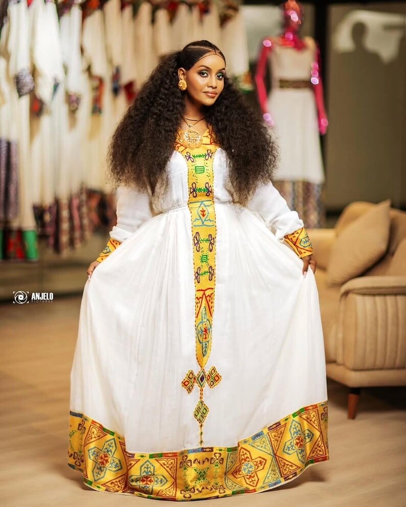 Woman wearing a Yellow Habesha Dress with colorful patterns in a clothing store.