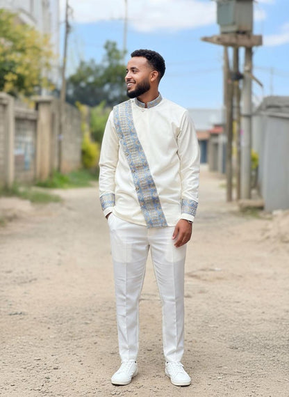 Man in a white Habesha Men's Outfit with a patterned sash standing on a street.