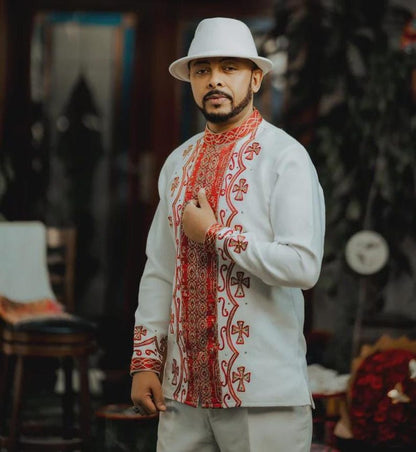 Man wearing a Red Ethiopian Cultural Men’s Shirt with red patterns and a white hat in an indoor setting.
