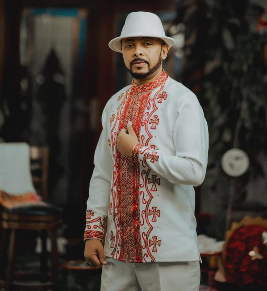 Man wearing a Red Ethiopian Cultural Men’s Shirt with red patterns and a white hat in an indoor setting.