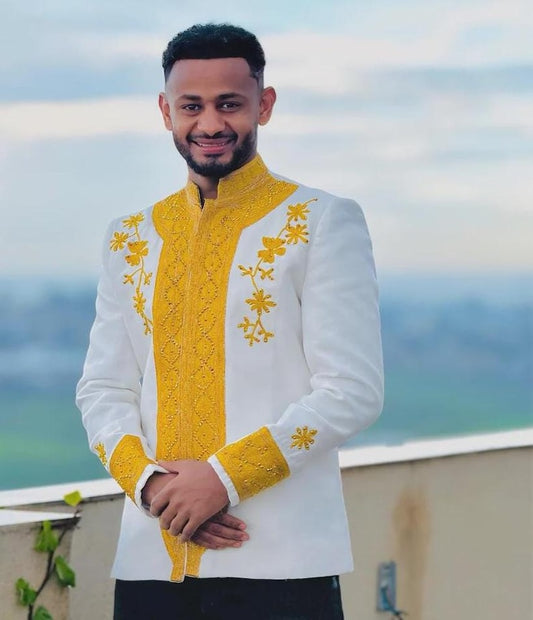 Man wearing a white and yellow embroidered Habesha Men’s Shirt with a scenic background.