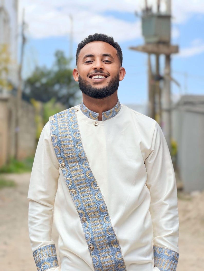 Man wearing a Habesha Men's Outfit with decorative patterns outdoors