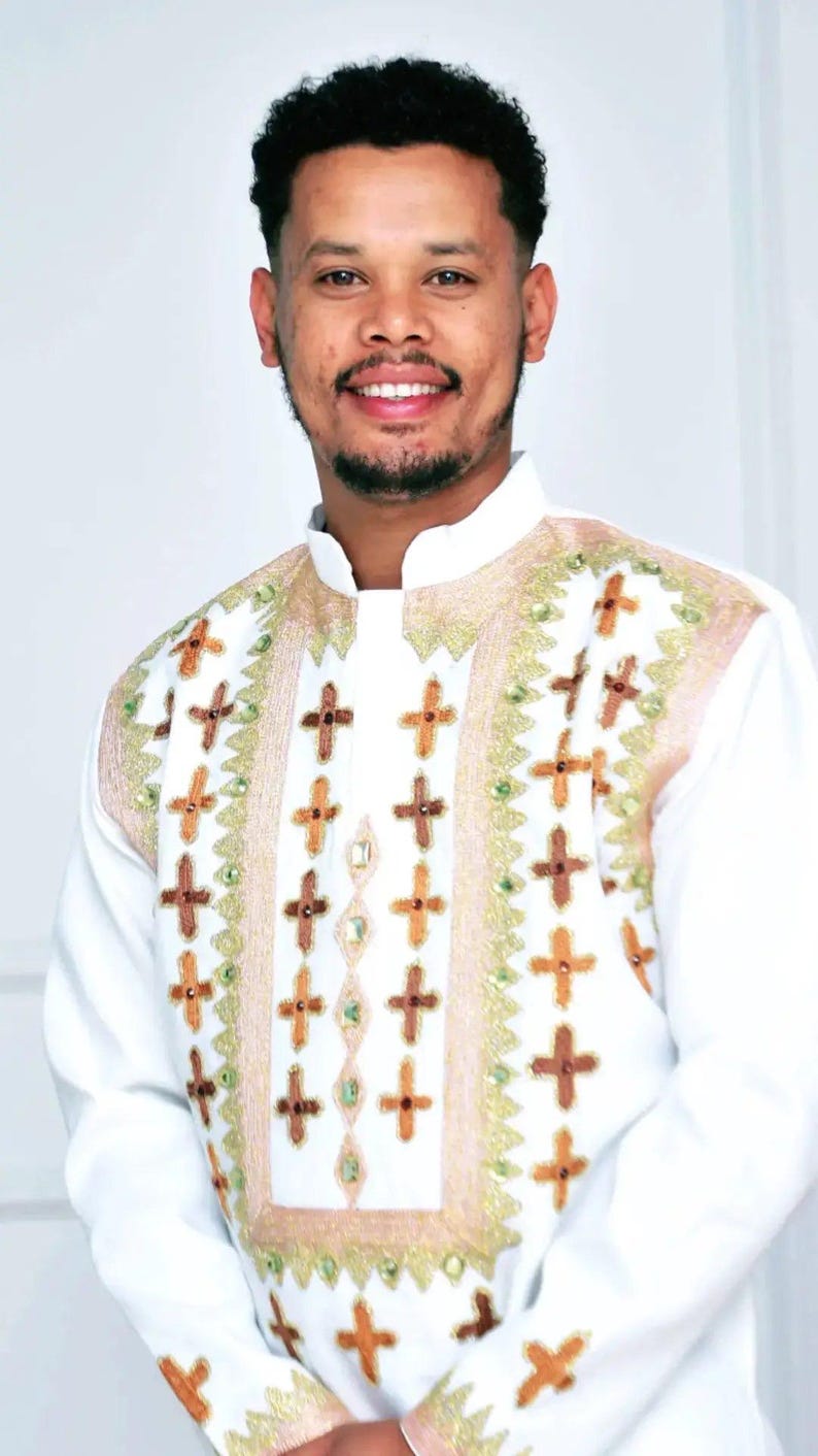 Man wearing a white embroidered Habesha Men’s Traditional Outfit with intricate patterns on a plain background
