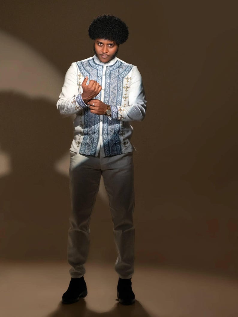 Person wearing in Ethiopian Men’s Shirt patterned jacket and light pants against a brown background