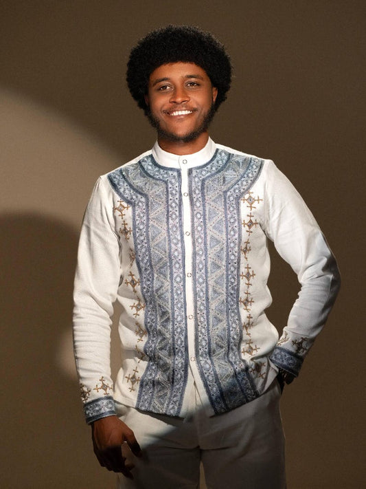 Man wearing a white Ethiopian Men’s Shirt with blue and gold embroidery against a brown background