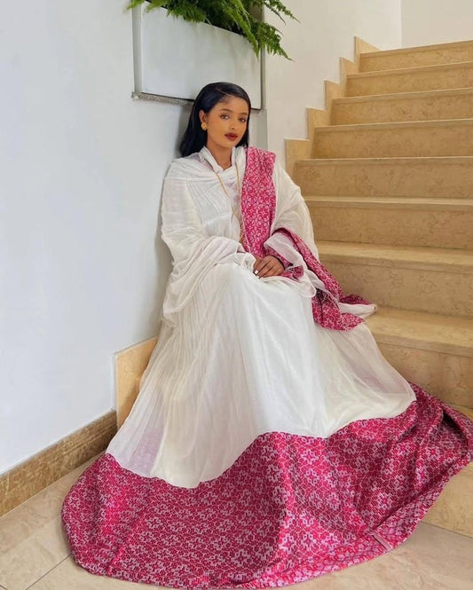 A woman wearing a traditional white Habesha kemis with a vibrant pink patterned shawl and a matching pink patterned hemline, sitting on beige stone stairs.