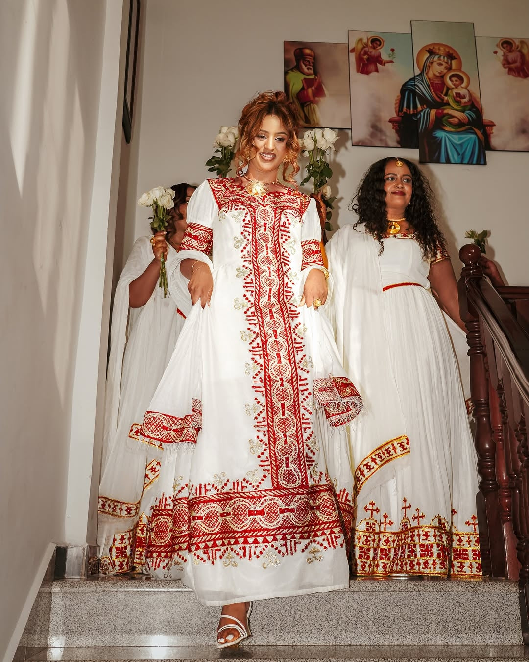 Woman in a white and red embroidered Traditional Eritrean Style  standing on a staircase with two other women.