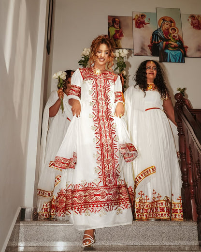 Woman in a white and red embroidered Traditional Eritrean Style  standing on a staircase with two other women.