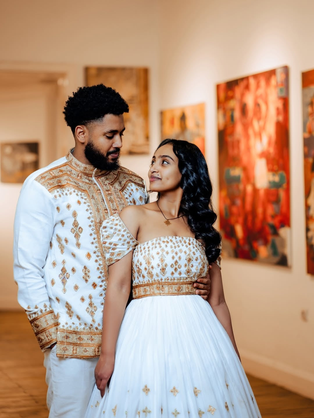 Couple in traditional Gold Unique Ethiopian Wedding Matching Couple Set for Her and Him –  standing in a room with artwork on the walls.