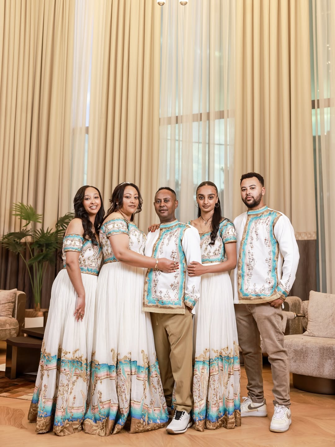 Family set in matching Ethiopian dress standing in a room with curtains and furniture.
