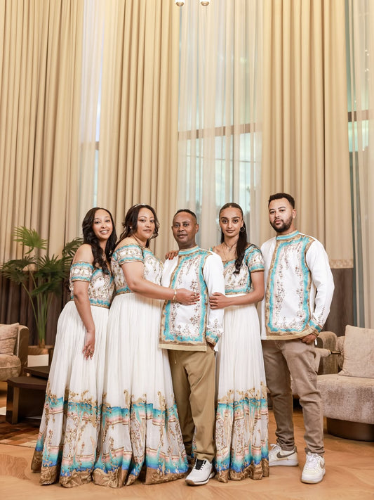 Family set in matching Ethiopian dress standing in a room with curtains and furniture.