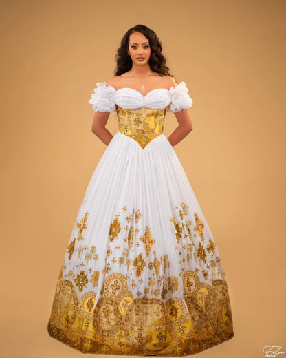 A woman modeling an off-the-shoulder ball Habesha Wedding Dress  with a white sweetheart bodice, puffed sleeves, and a full white skirt decorated with ornate gold baroque-style patterns, set against a solid tan background.