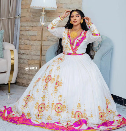 A woman seated in a light blue armchair wearing an ornate white traditional Habesha wedding dress with bright pink and gold embroidery, a matching pink belt, and a large embroidered skirt. She is posed indoors against a stone wall and lamp, with a watermark reading “@林婉B” visible on the dress.