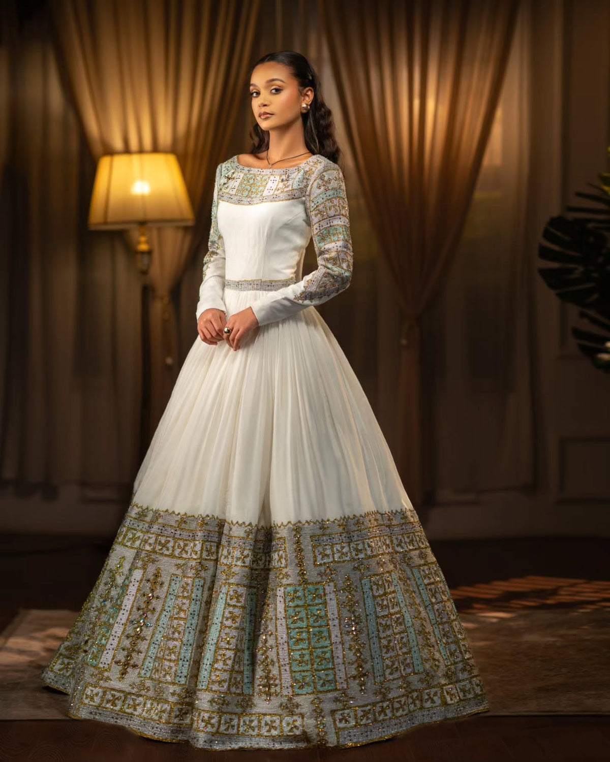 Woman wearing a white and gold embroidered Habesha Wedding Dress  in a warm-toned room.