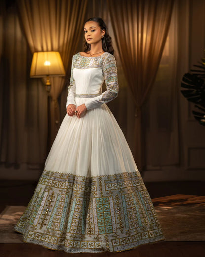 Woman wearing a white and gold embroidered Habesha Wedding Dress  in a warm-toned room.