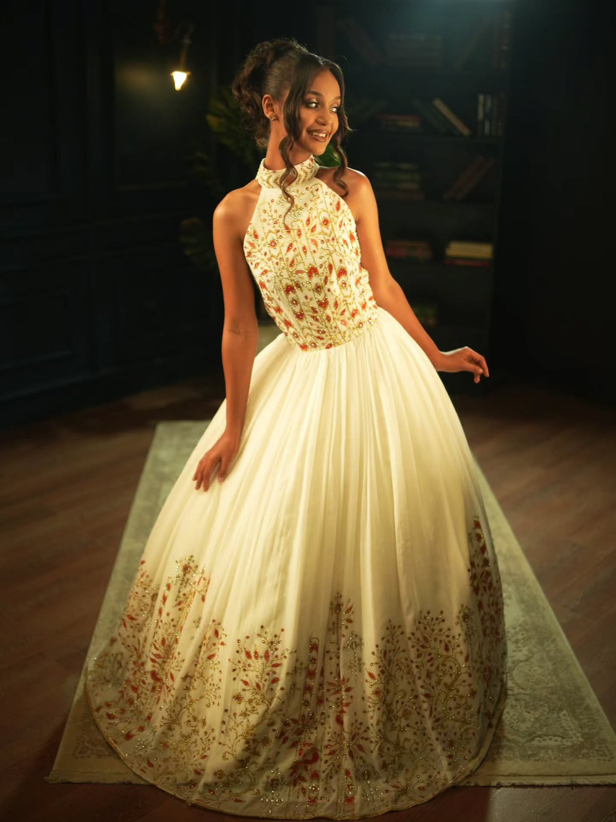 A young girl modeling a cream ball Habesha Wedding Dress with intricate floral embroidery in red, gold, and green, set against a dark, elegant indoor background.