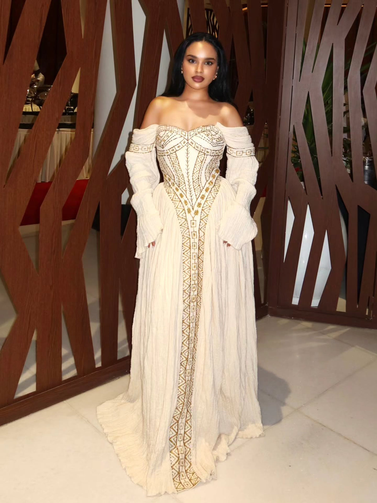 Woman in an elegant off-shoulder  Habesha Wedding Dress  with intricate designs standing indoors.