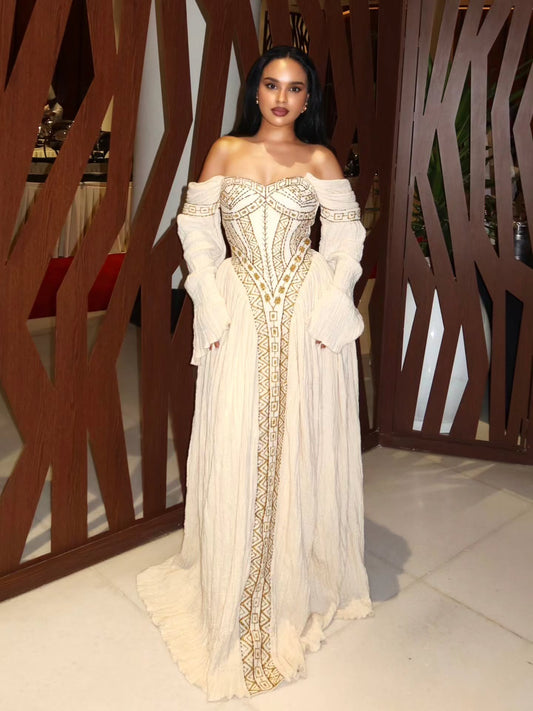 Woman in an elegant off-shoulder  Habesha Wedding Dress  with intricate designs standing indoors.