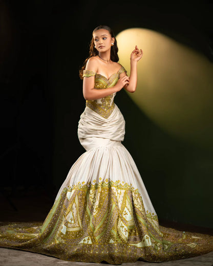 A model wearing a dramatic off-the-shoulder white Habesha Wedding Dress  with gold embroidery and a long train, posed against a dark background with a spotlight.