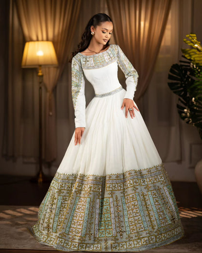 Woman wearing a white and gold embroidered traditional Habesha Wedding Dress  in a warm-toned room.