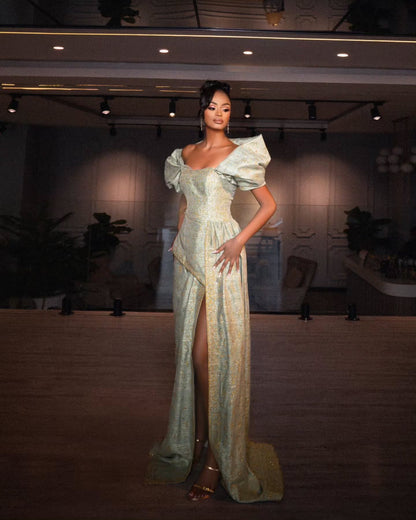 A model stands on a runway wearing a floor-length sage green Habesha Wedding Dress with dramatic puffed off-the-shoulder sleeves, a high thigh slit, and a subtle gold-toned pattern.
