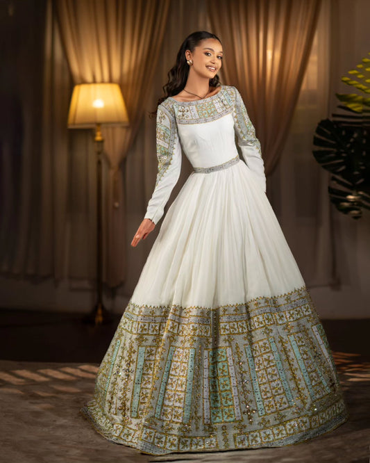 Woman wearing a white and gold embroidered Habesha Wedding Dress  in a warm-toned room.
