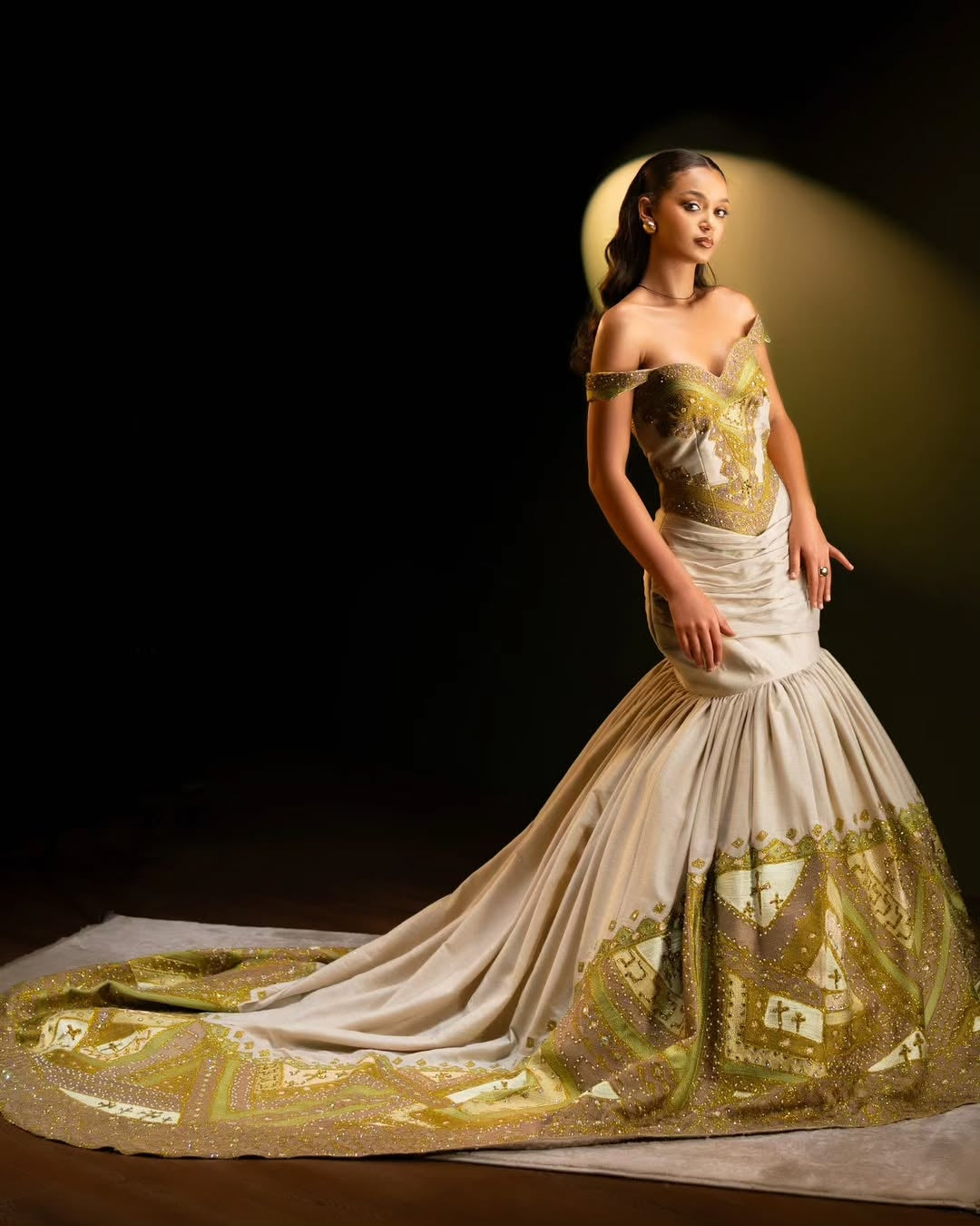 Woman wearing a white and gold Green Mermaid Ethiopian Dress with intricate designs on a dark background