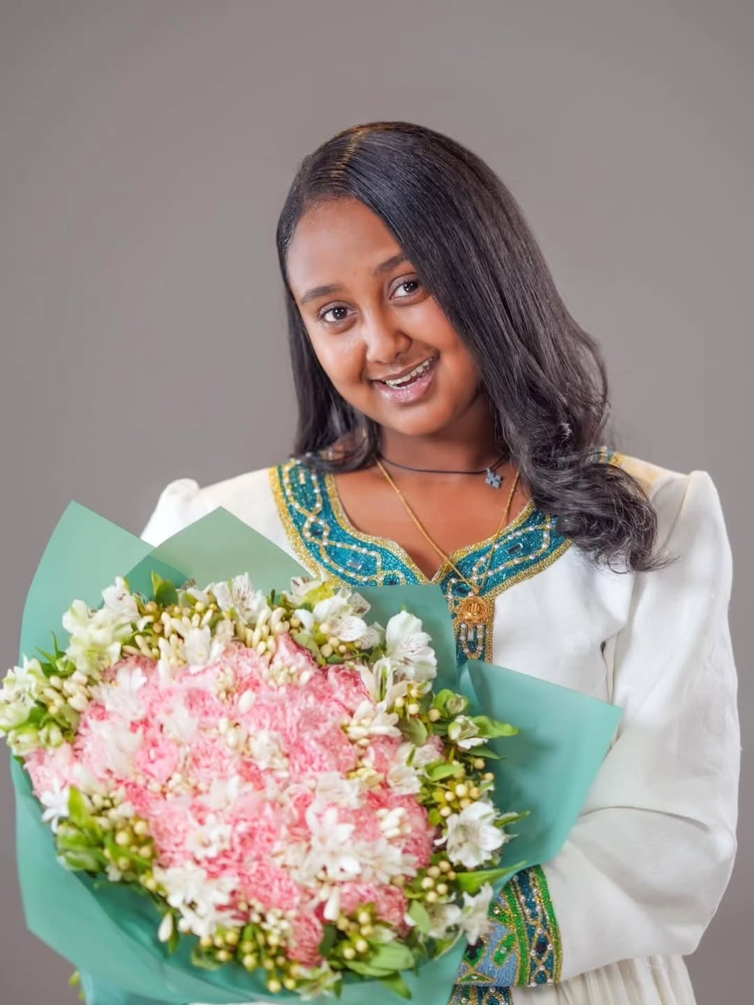 Woman wearing Green Habesha Kemis holding a bouquet of flowers against a plain background