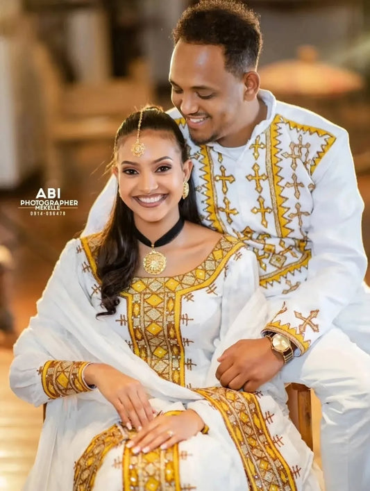 Couple in traditional white and gold embroidered outfits sitting together.