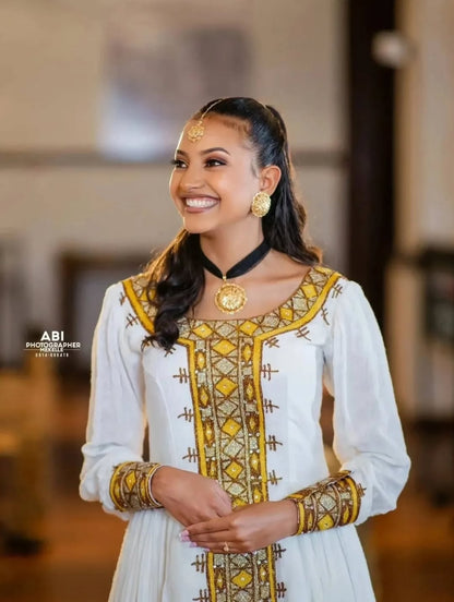 Woman in traditional attire with gold and yellow patterns, smiling indoors.