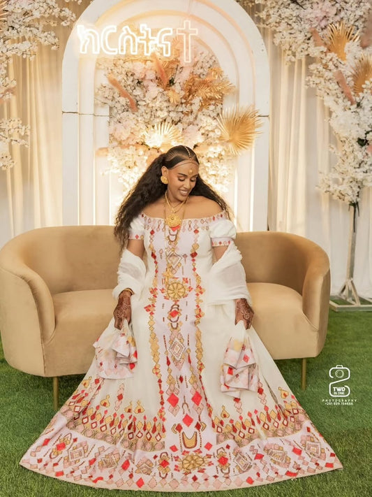 Woman in a decorative habesha dress sitting on a couch with floral and arch decorations in the background