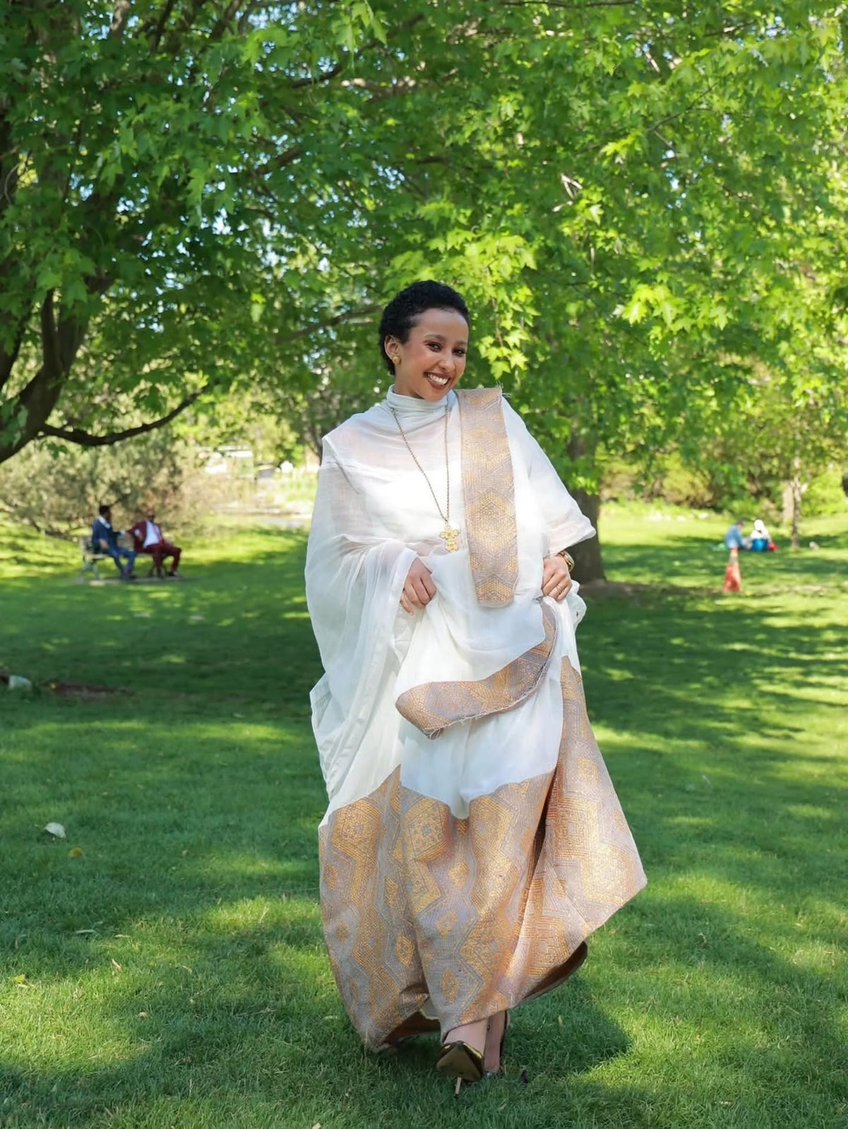 Woman in a traditional Habesha Kemis  standing in a park with green trees and grass.