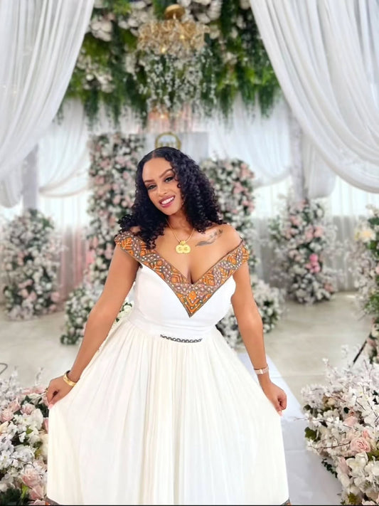 Woman in a white habesha zuria with decorative top in a decorated indoor setting