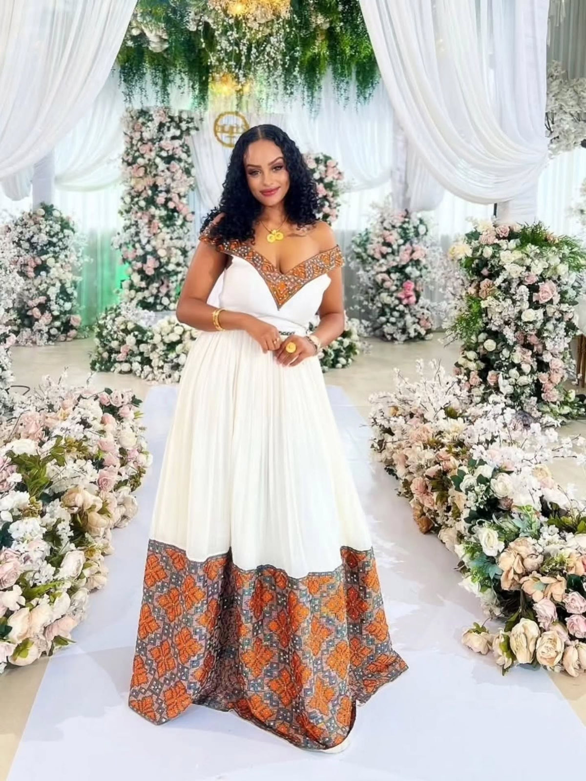 Woman in a white and patterned habesha zuria standing in front of floral decorations