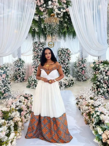Woman in a white and patterned habesha dress standing in a decorated indoor setting with flowers and white drapes.