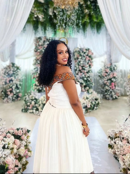 Woman in a white habesha zuria standing in front of floral decorations