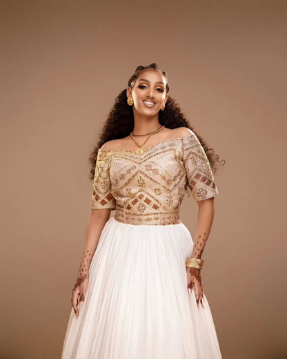 Woman wearing a traditional Habesha Kemis with a gold top and white skirt on a brown background
