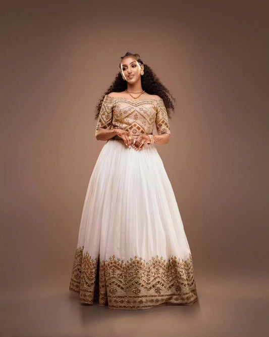 Woman wearing a gold and white traditional Habesha Kemis on a brown background